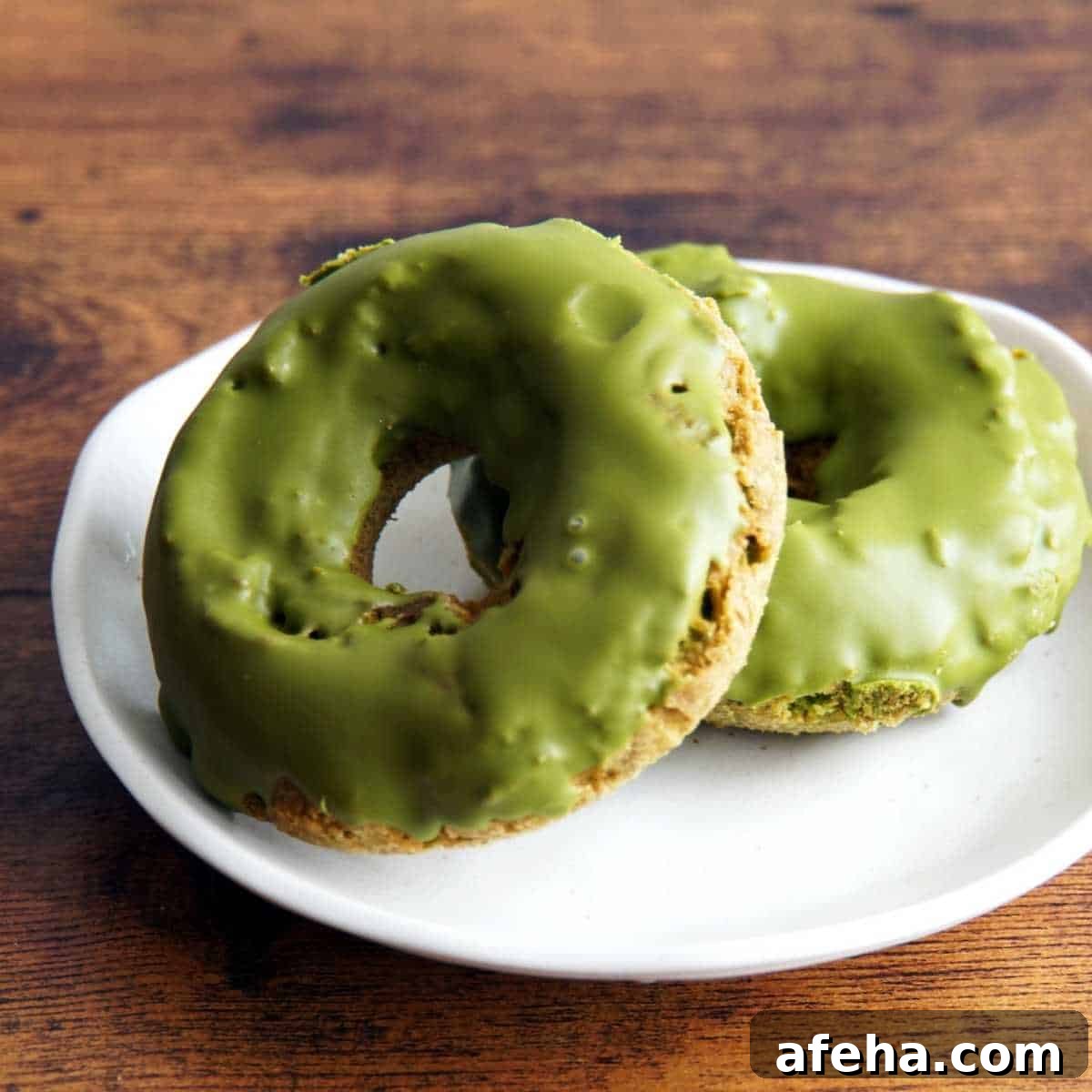 Two matcha baked doughnuts with matcha glaze on a white plate.