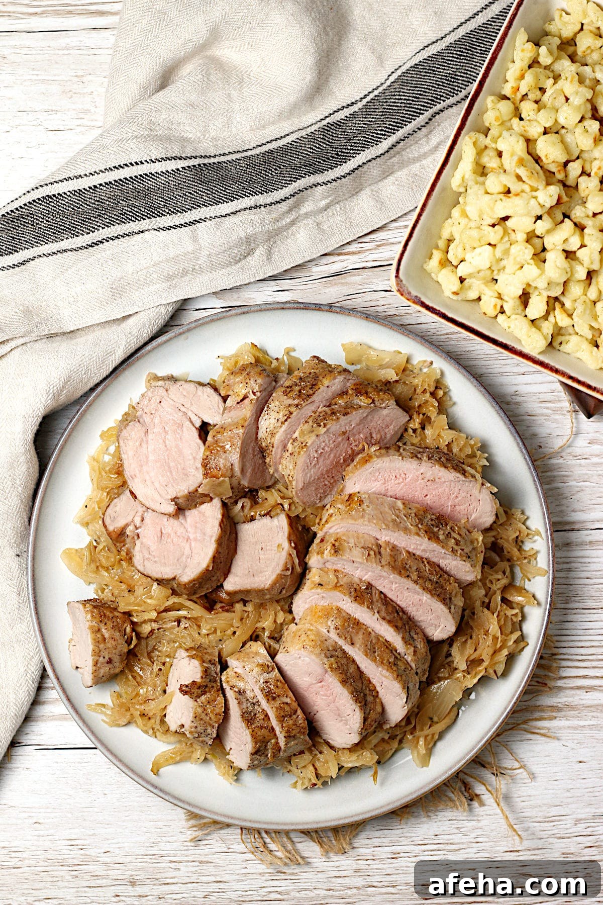 Overhead photo of sliced pork tenderloin sitting on a bed of sauerkraut on a large plate.