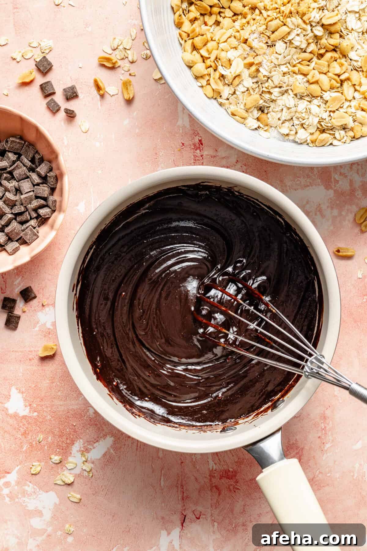 a pot of melted chocolate with chocolate chips and salted peanuts on a light pink background