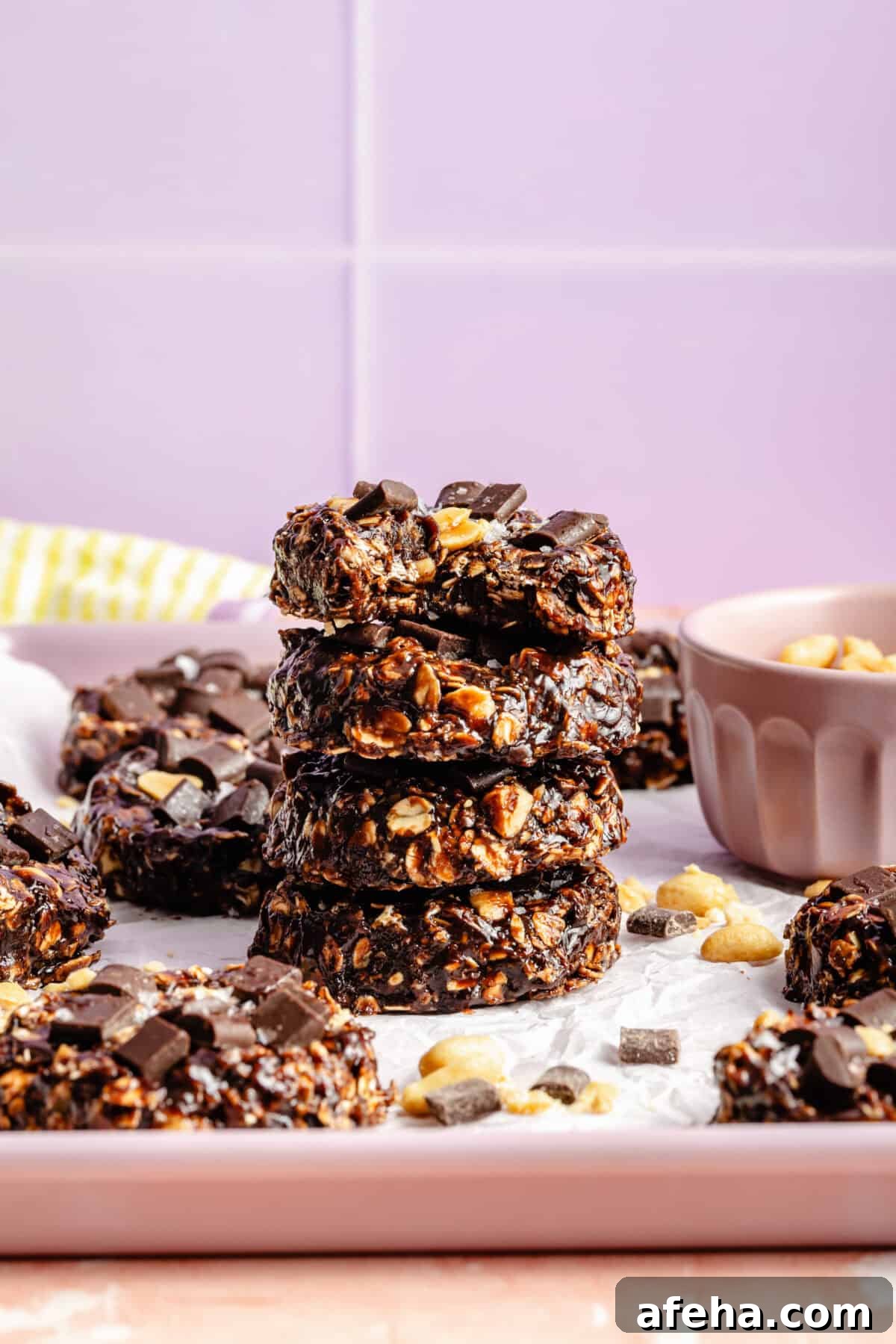 a stack of chocolate and oat cookies with salted peanuts on a light purple background
