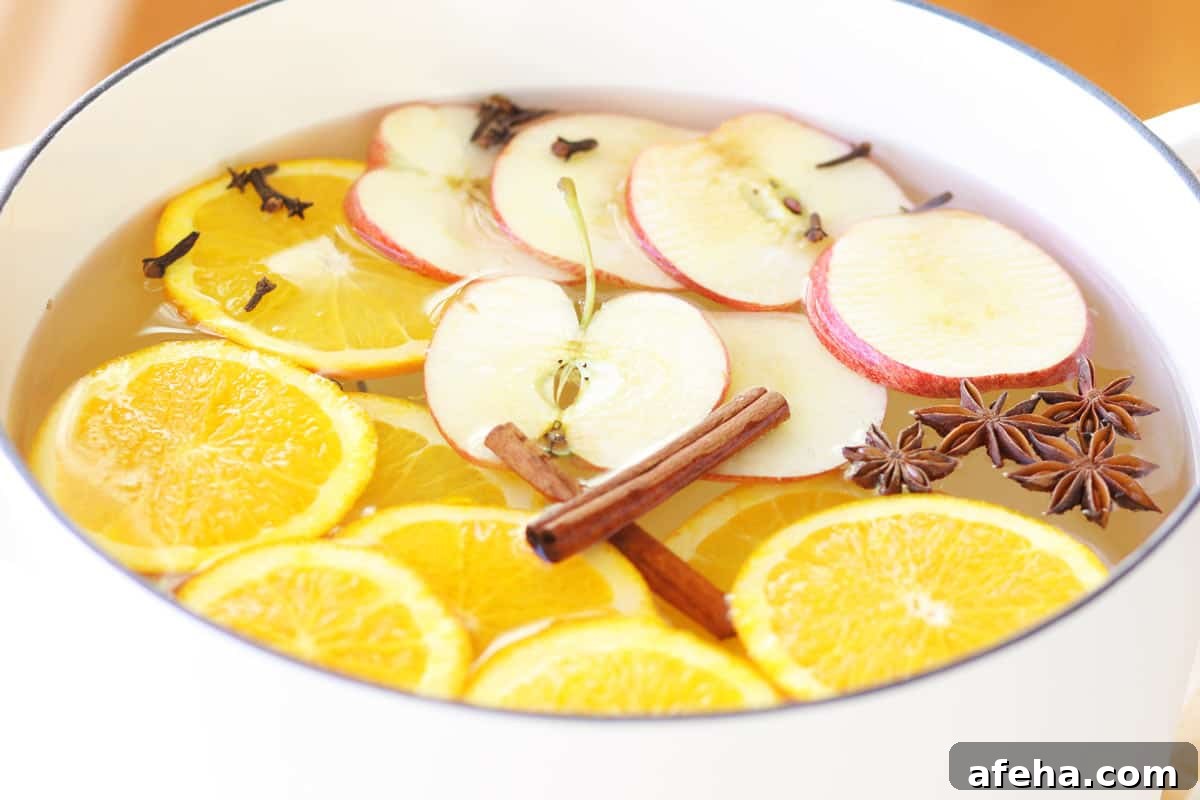 a white dutch oven with a striped yellow and white towel under it. It is filled with water and a fresh homemade potpourri made of oranges, apples and spices.
