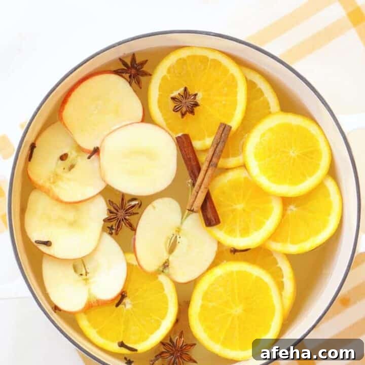a white dutch oven with a striped yellow and white towel under it. It is filled with water and a fresh homemade potpourri made of oranges, apples and spices.