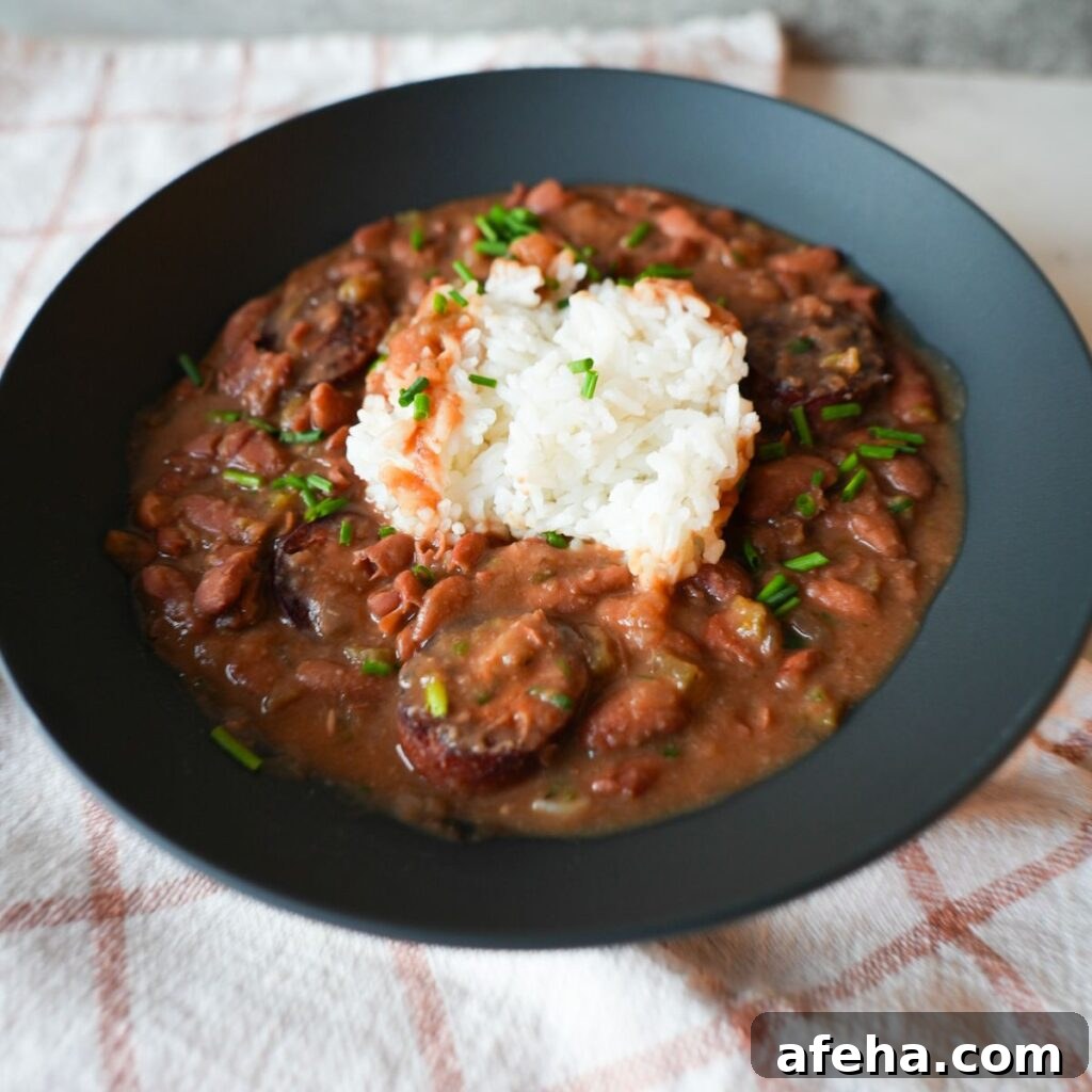 Authentic Red Beans and Rice Recipe for Weeknight Comfort Meal 2 Bowl of red beans and rice with sliced sausage, garnished with chopped chives and parsley on top of fluffy white rice.