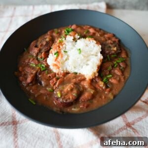 Authentic Red Beans and Rice Recipe for Weeknight Comfort Meal 7 Bowl of red beans and rice with sliced sausage, garnished with chopped chives and parsley on top of fluffy white rice.