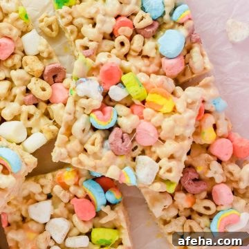 stacked lucky charm rice krispie treats cut into squares on white parchment.