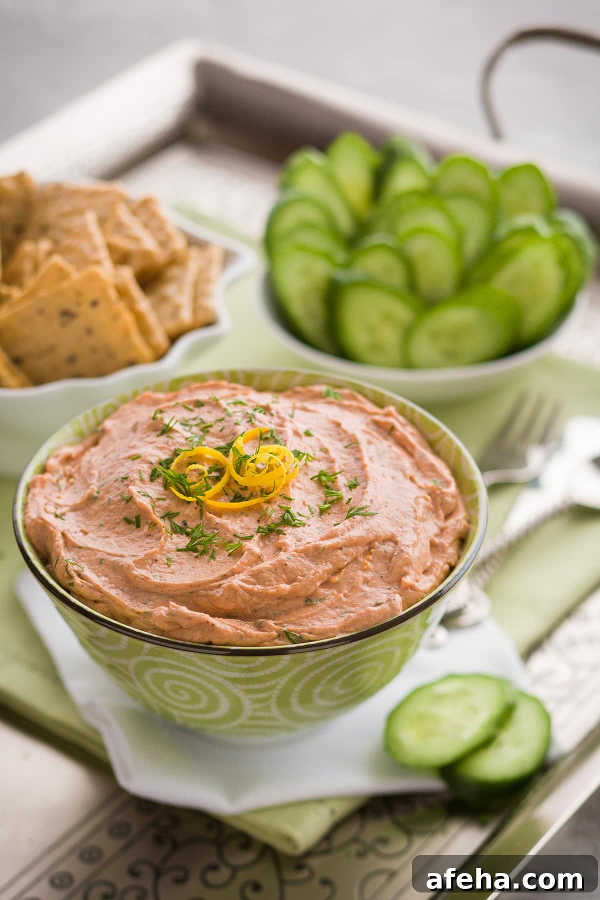 Creamy pale orange smoked salmon dip on a tray with cucumber slices and crackers.