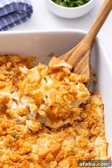 A wooden spoon scoops million dollar chicken casserole from the baking dish.