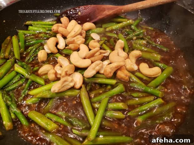 Roasted cashews are added to the asparagus cashew stir fry in the skillet.