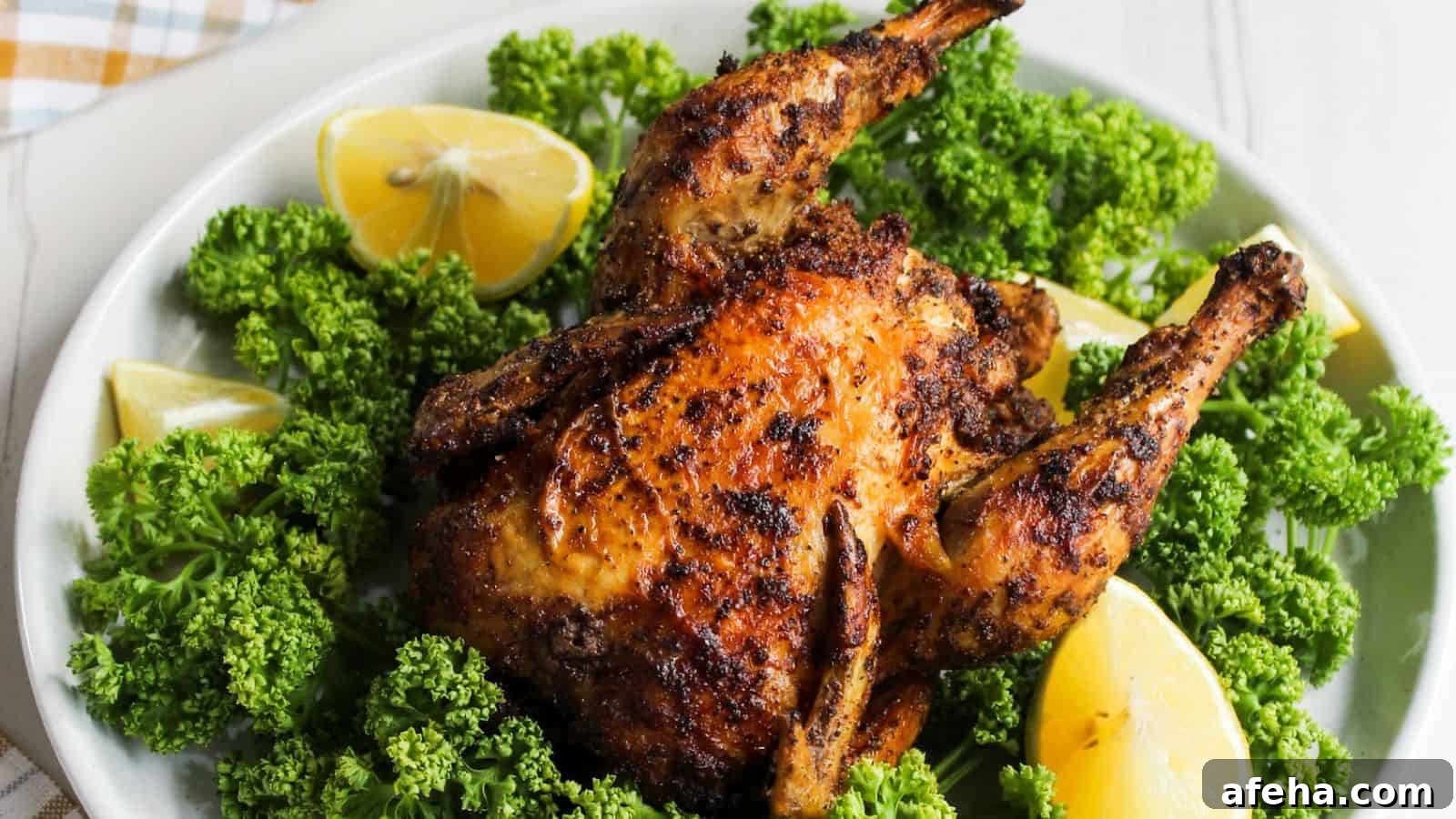 Air fryer Cornish hen on a white plate with lemon wedges.