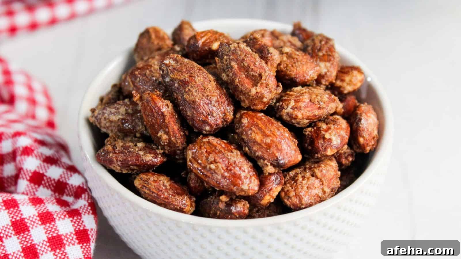 A bowl of candied almonds on a wooden table, with a red and white checkered napkin partially visible.