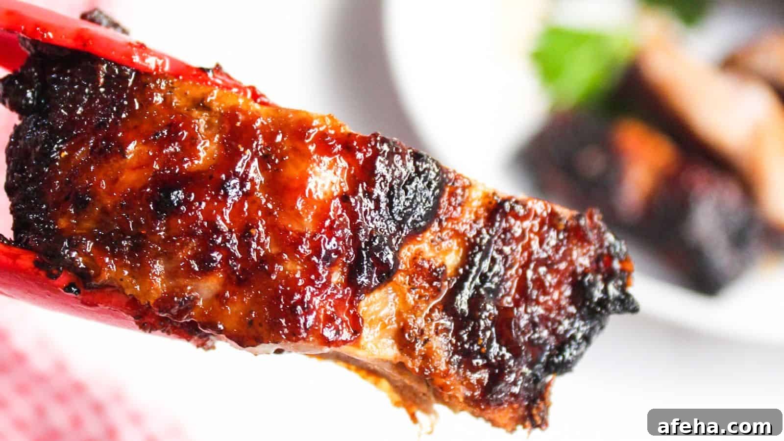 Close-up of an air-fried barbecued rib with charred edges over a white plate.