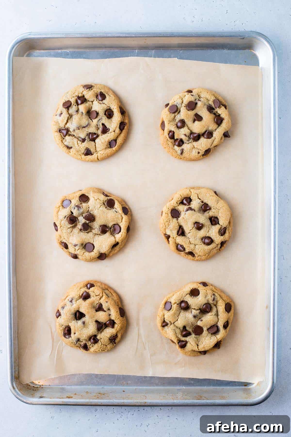 Overhead view of 6 chocolate chip cookies on parchment-lined baking sheet