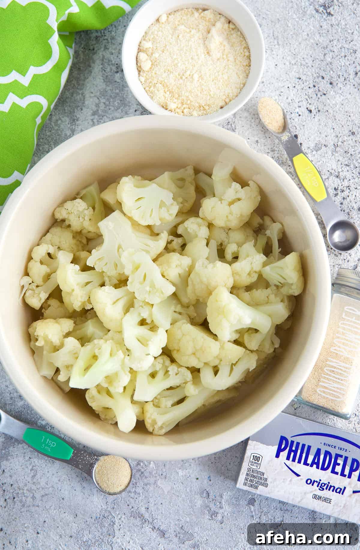 A bowl of steamed cauliflower is placed next to other ingredients. 