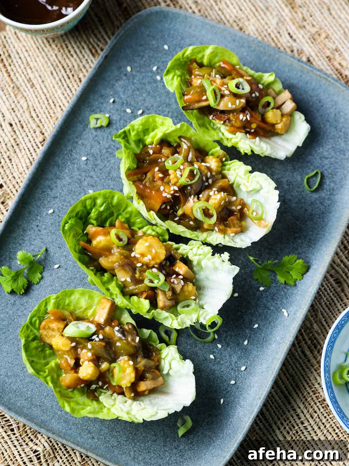Vegan San Choy Bau Recipe: Flavorful Plant-Based Lettuce Wraps 3 Overhead photo of vegan san choy bau in lettuce leaves on a blue-grey oblong plate on a jute mat underneath.