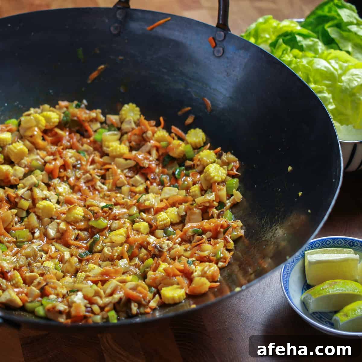 Vegan San Choy Bau Recipe: Flavorful Plant-Based Lettuce Wraps 4 Photo of vegan san choy bau filling cooked in a wok, with a plate of lettuce leaves to the side and some lime wedges.