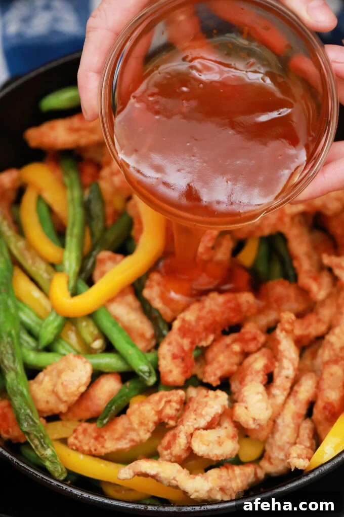 Adding honey sesame sauce to fried chicken strips with green beans and bell pepper.