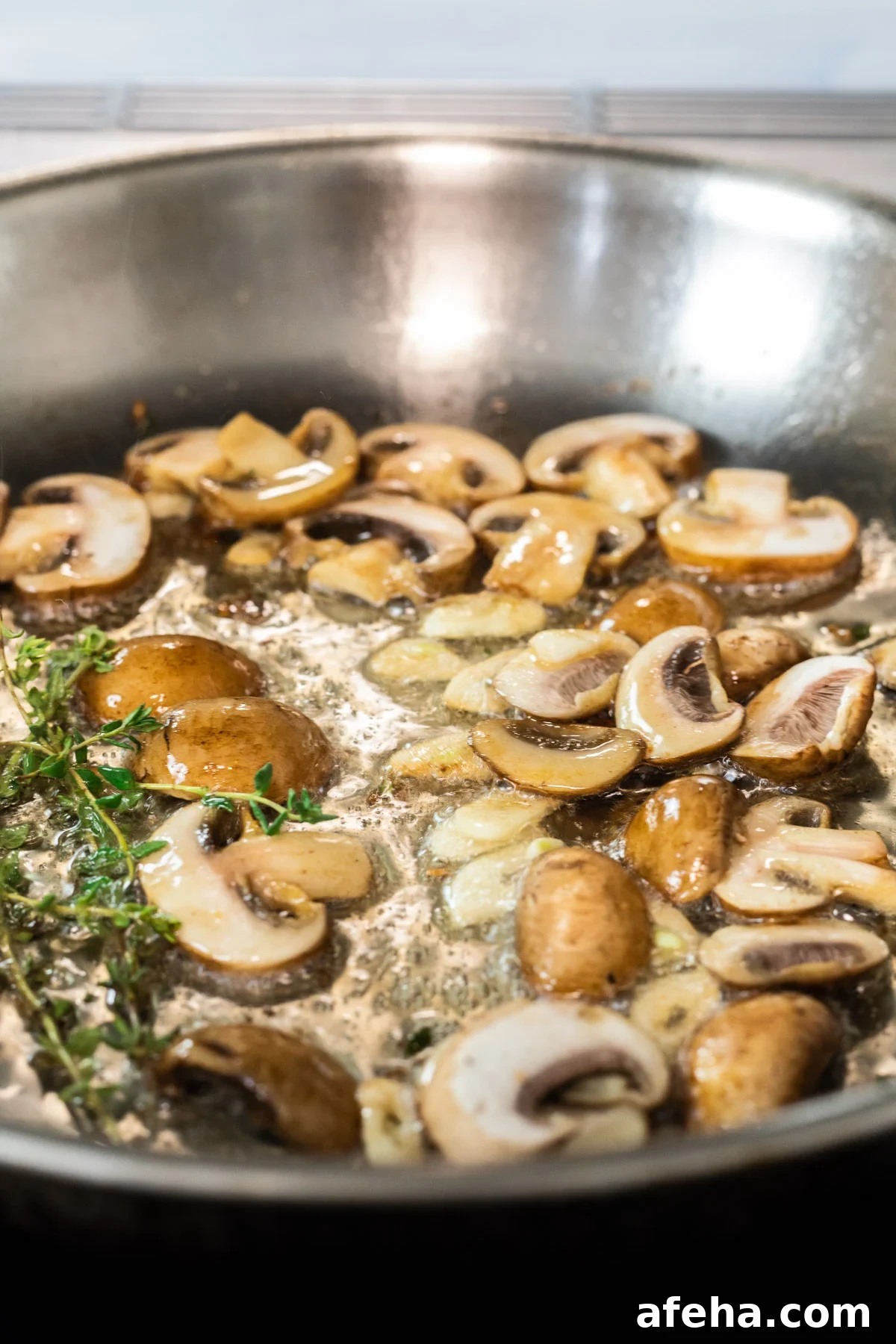 Sliced mushrooms cooking in a skillet with garlic and thyme.