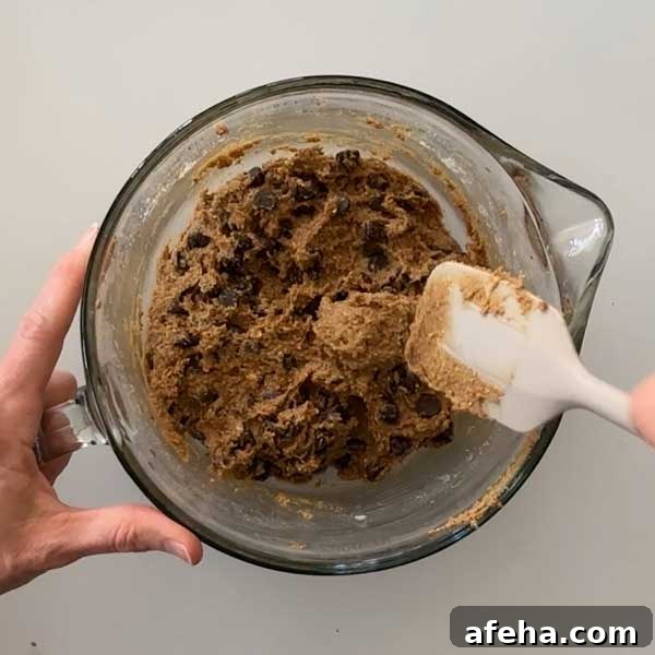 Folding the chocolate chips into the cookie dough batter with a spatula.