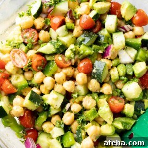 close up of chickpea salad showing chickpeas, cucumbers, tomatoes, and creamy salad dressing