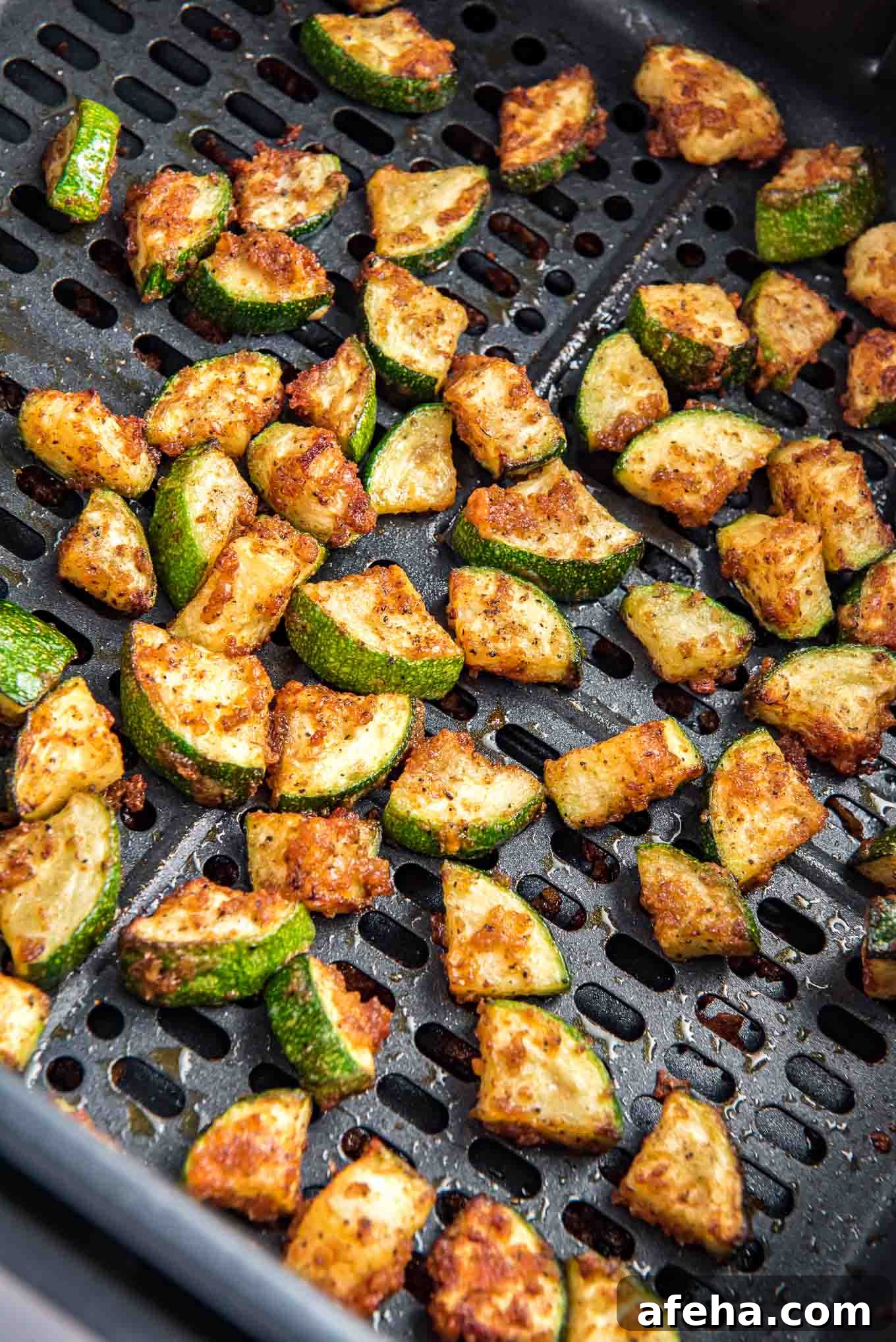 Zucchini in the air fryer basket after cooking with browned edges.