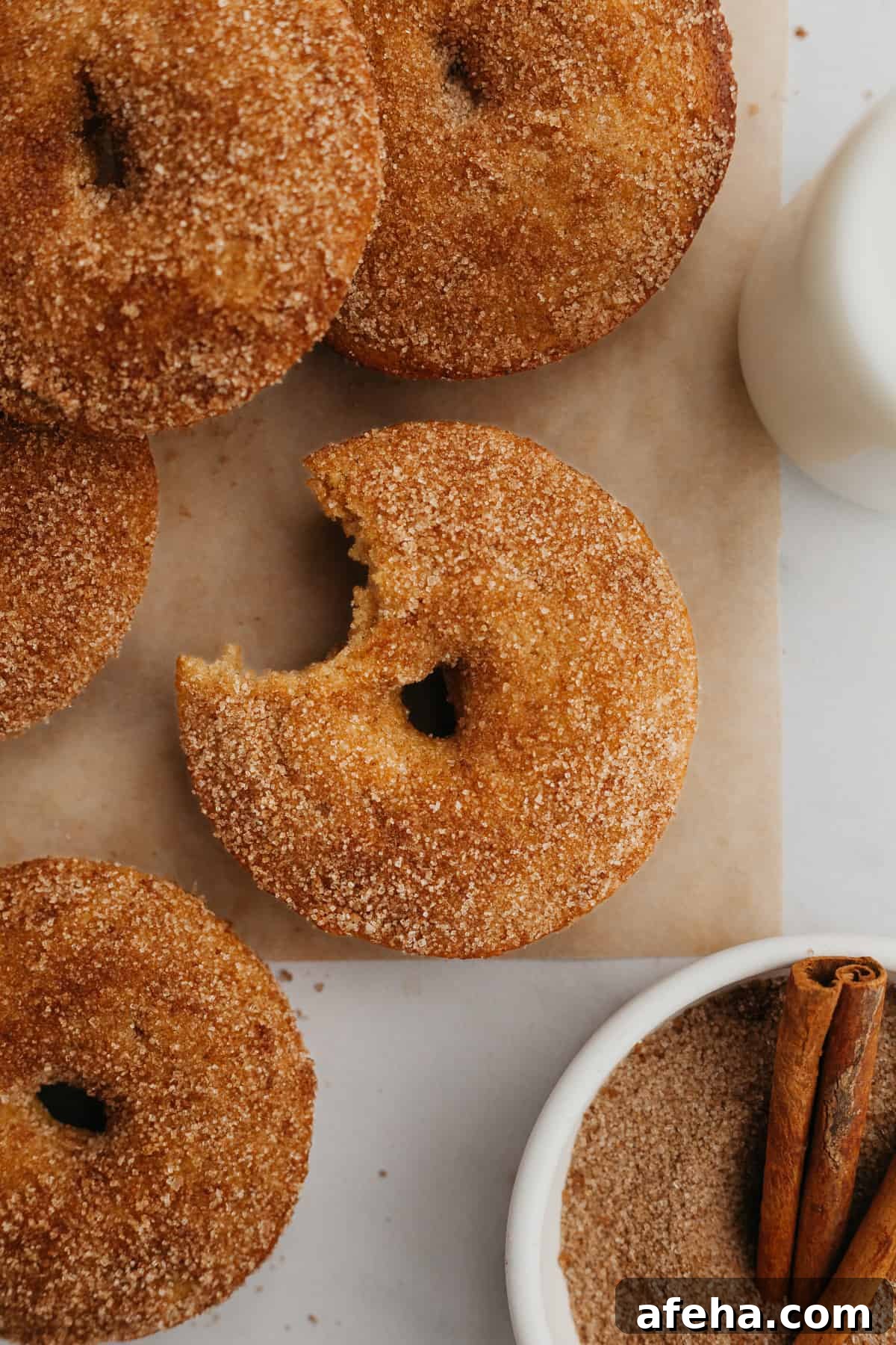 A close up of baked cinnamon sugar donuts, one has a bite taken out of it.