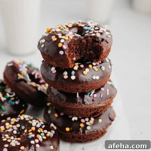 a stack of chocolate sprinkle donuts, the donut on top has a bite taken out of it.