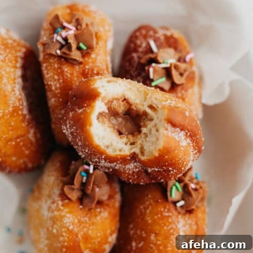 Five brioche doughnuts on top of parchment paper. One doughnut is on top, a bite taken out of it showing a chocolate filling