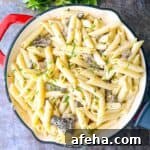 A beautifully presented skillet of Morel Mushroom Pasta, with a wooden spoon ready to serve the dish, and a sprinkle of fresh parsley on top.