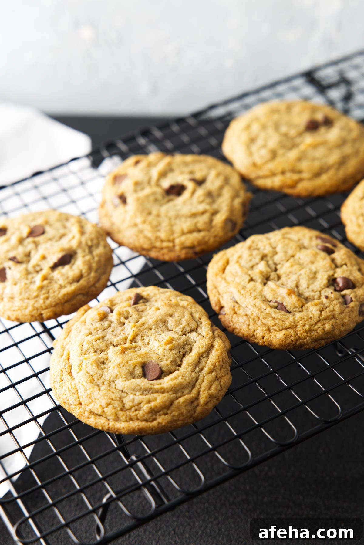 Six chocolate chip banana bread cookies cooling on a wire rack with white parchment paper on the table beneath.