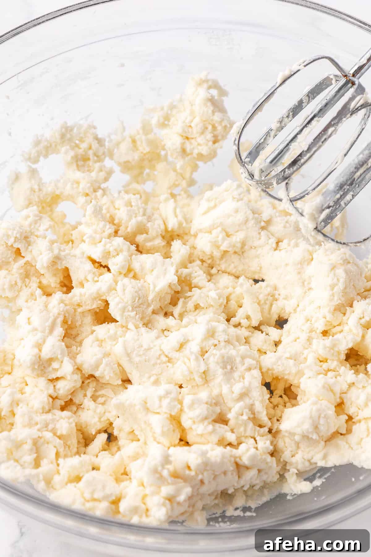 dough for butter mints in a clear glass bowl with mixer tools leaning on the side