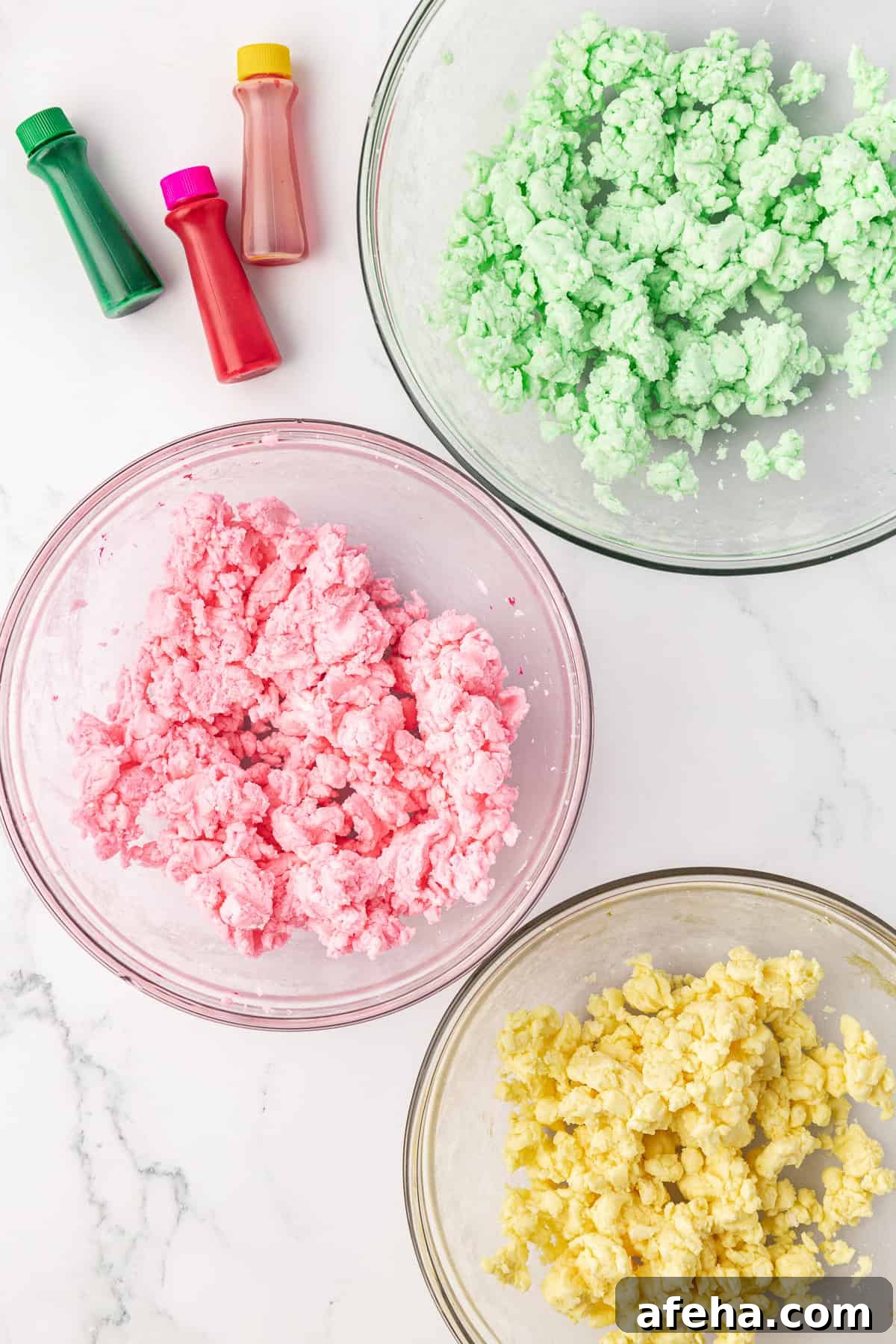 over head view of three glass bowls with butter mint dough and three different colors of food coloring: green, pink, and yellow