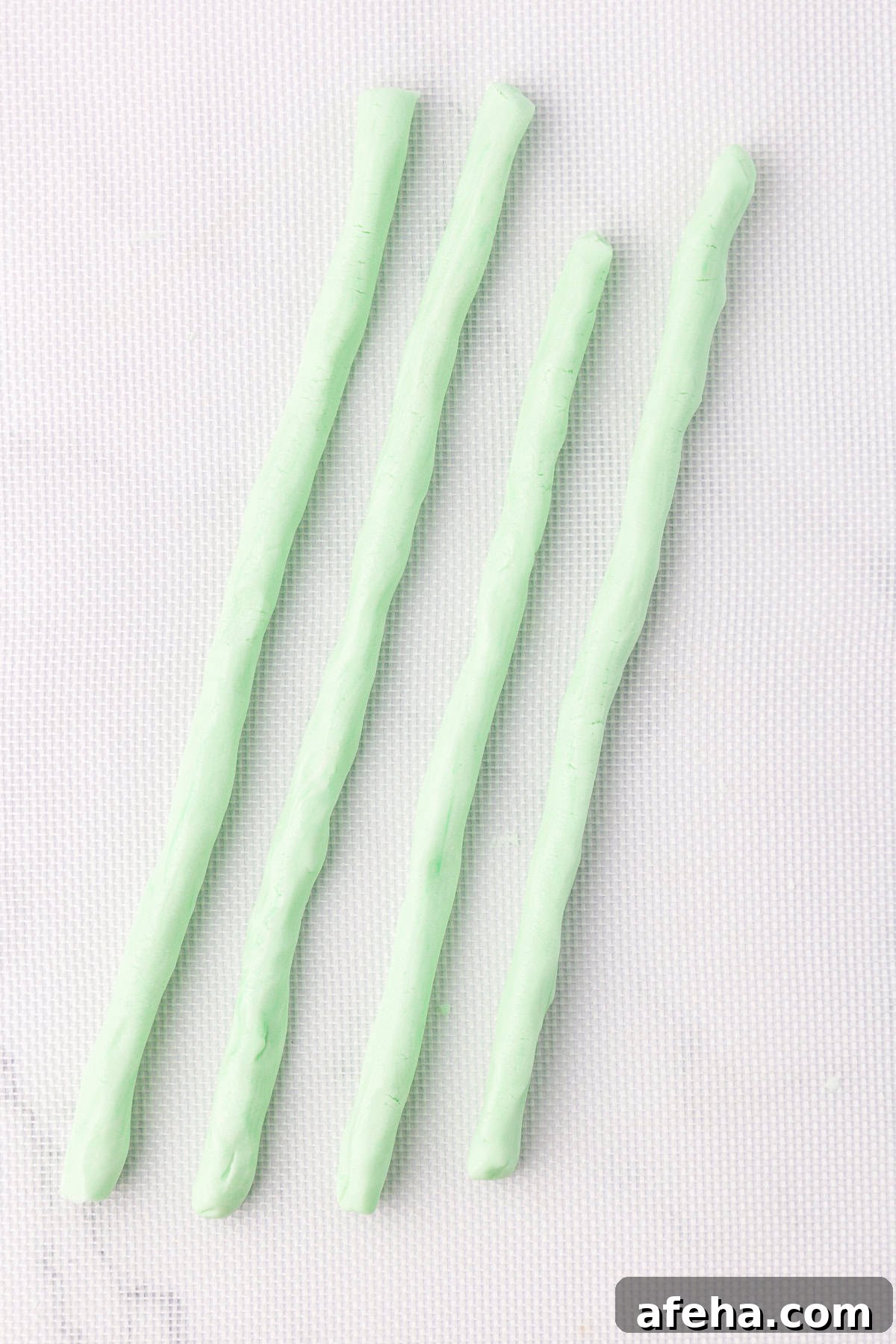 4 light green ropes of butter mints not yet cut, laying on a white silicone mat
