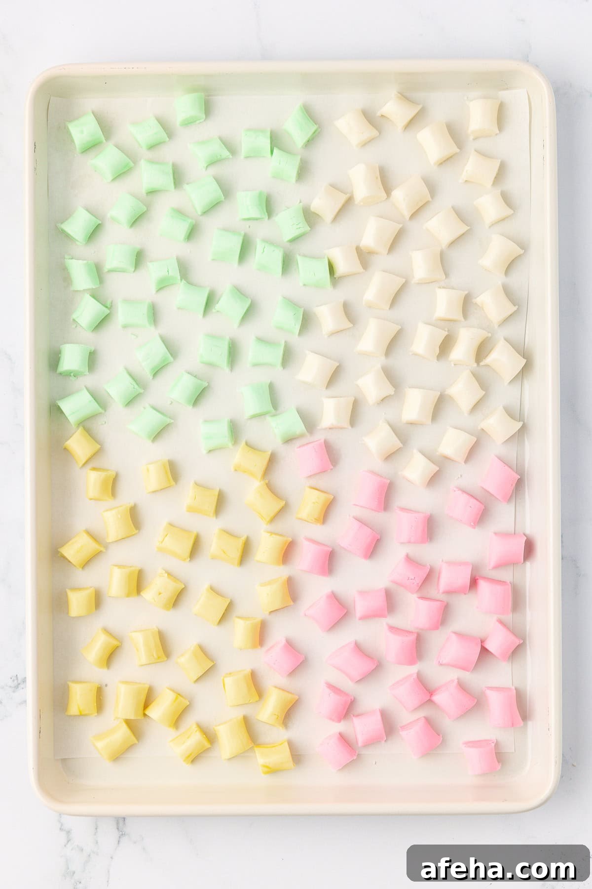 over head view of a sheet pan with spread out green, white, yellow, and pink butter mints drying on it