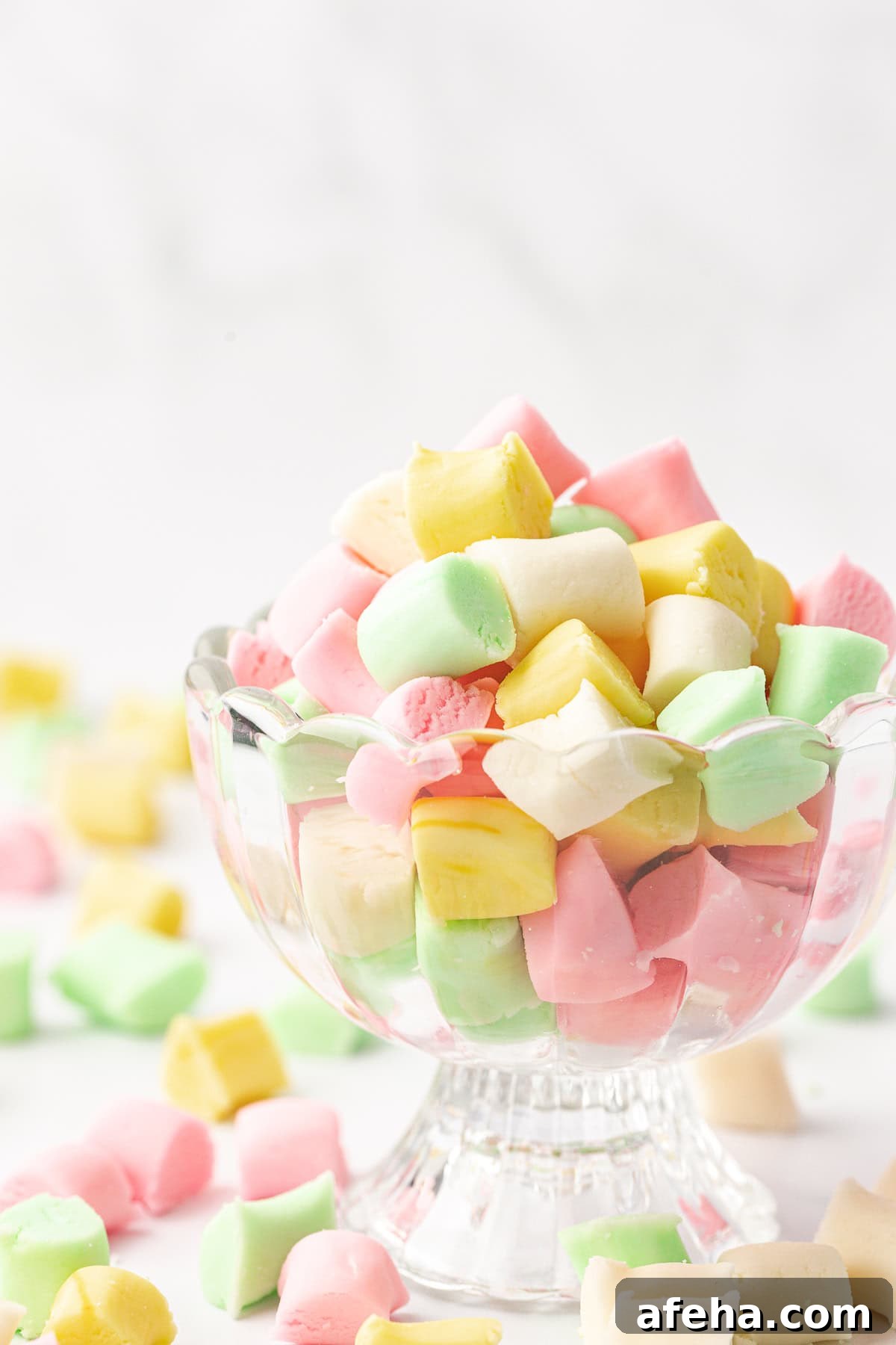 glass trifle dish full of white, green, pink and yellow butter mints with more mints scattered around