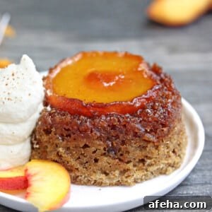 Single Peach Upside-Down Cake on a white plate next to whipped cream and peach slices.