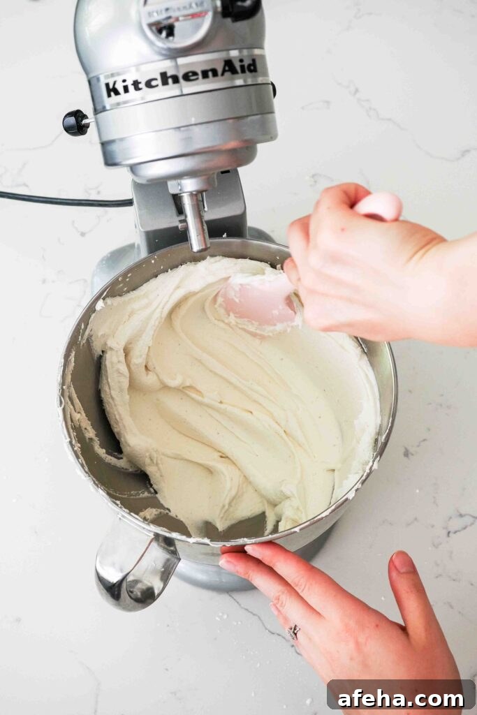 A spatula presses buttercream against the side of a bowl to remove any large air bubbles.