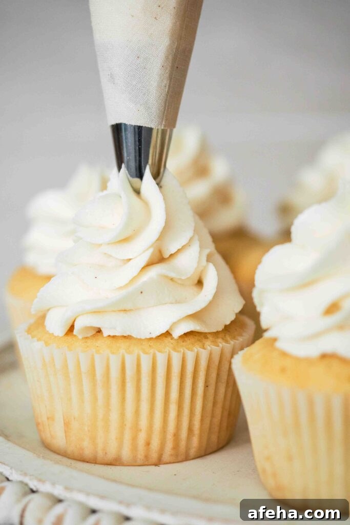 Vanilla bean buttercream is piped onto a vanilla cupcake.