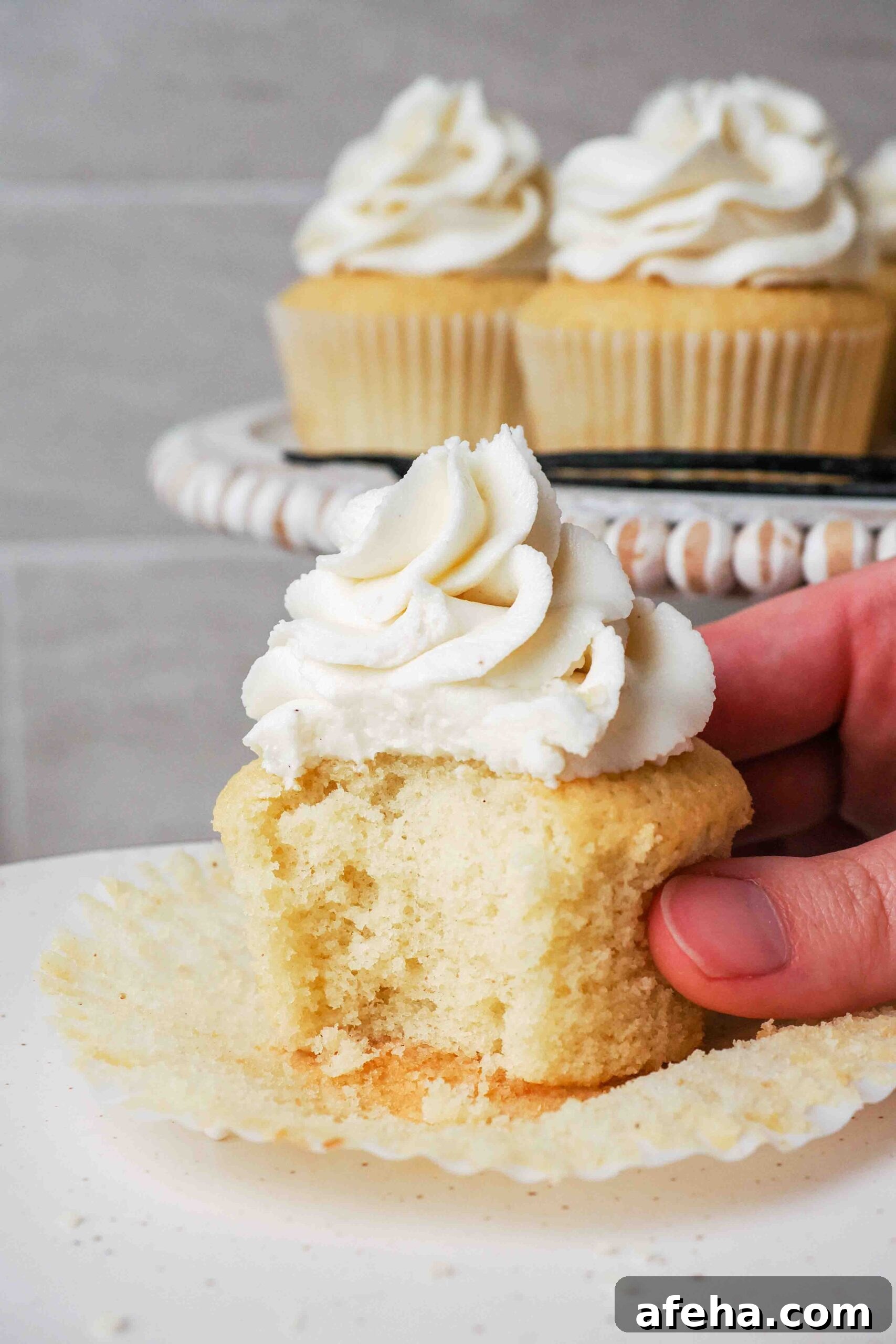 A hand holds a half-eaten vanilla bean cupcake.