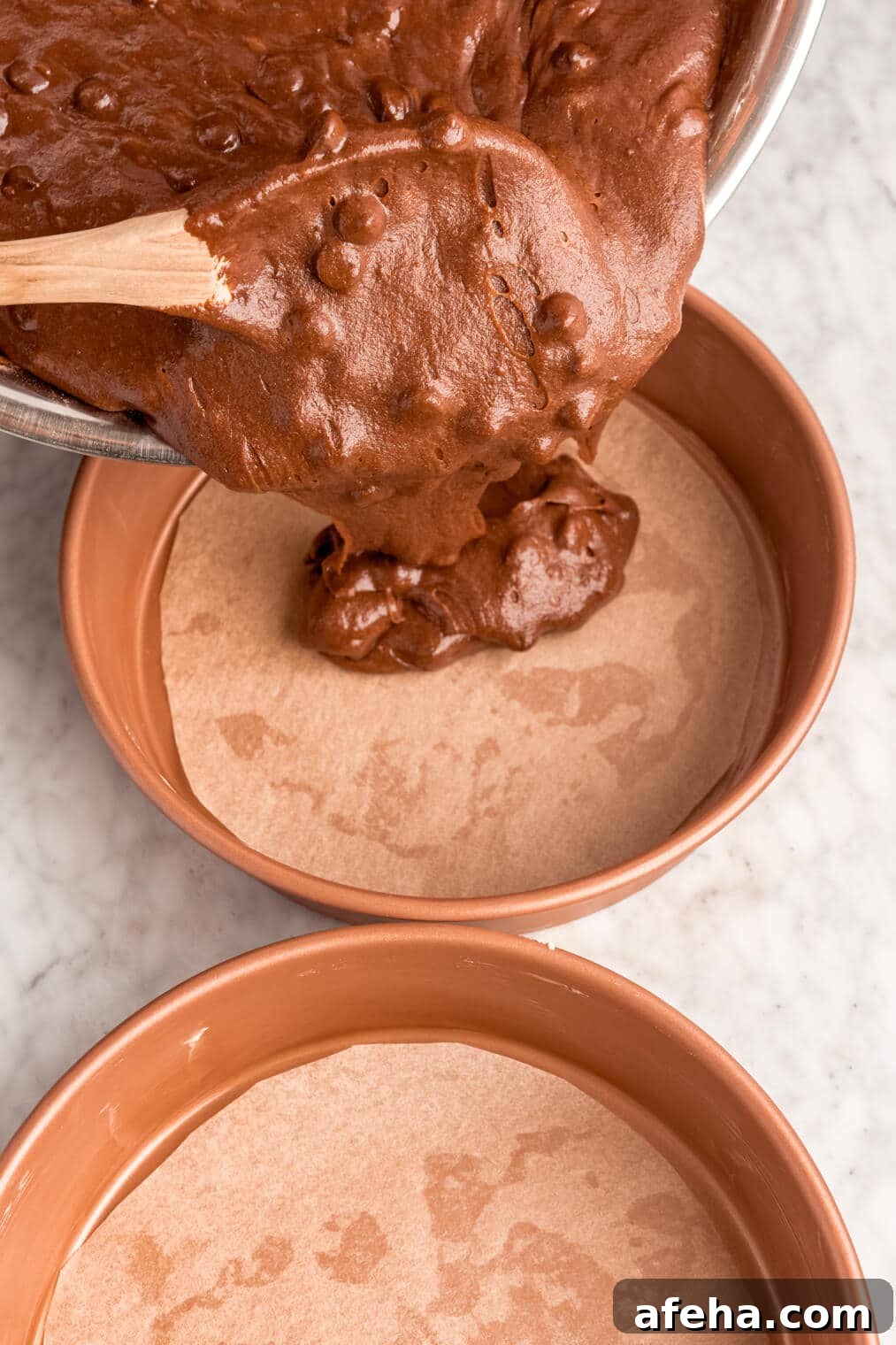 Chocolate cake batter being poured into a round cake pan lined with parchment paper on the bottom.