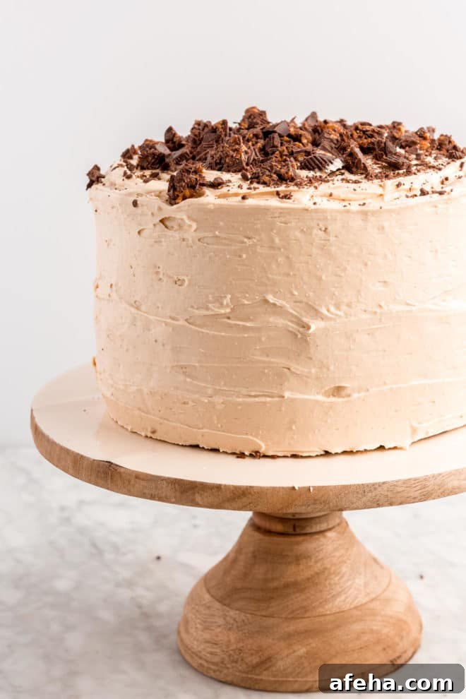Double layer cake coated with peanut butter buttercream and topped with shaved peanut butter cups on a cake stand.