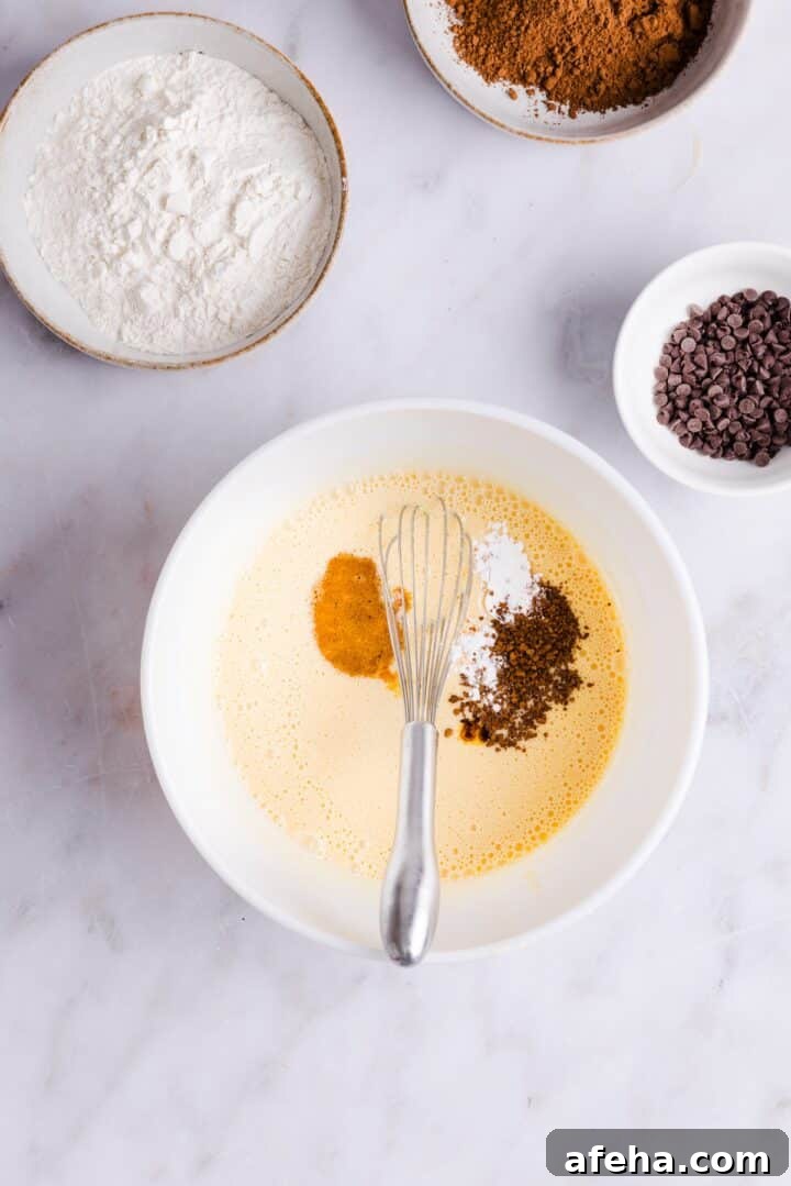 Ingredients for cottage cheese brownies being added to a blended cottage cheese mixture in a large white bowl