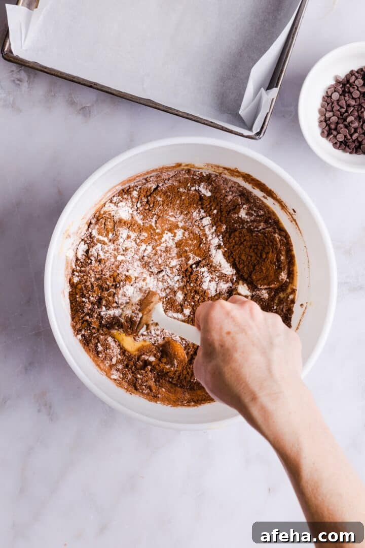 Brownie batter being stirred in a large white bowl by a woman's hand