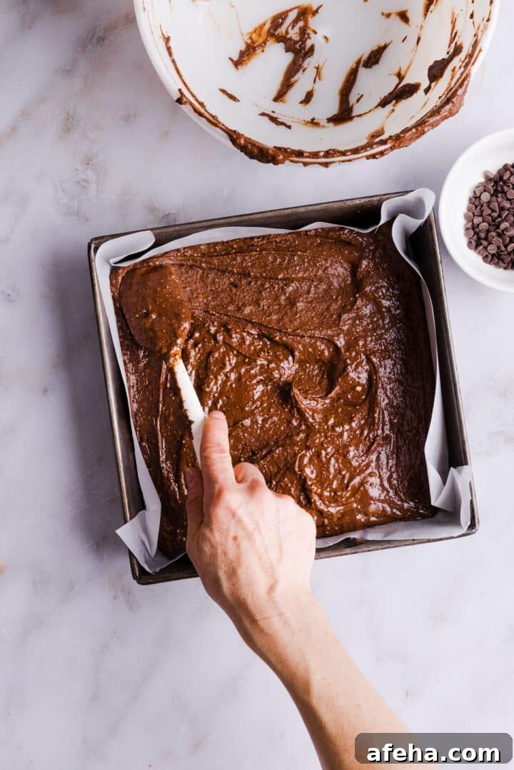Brownie batter being spread in a square brownie pan