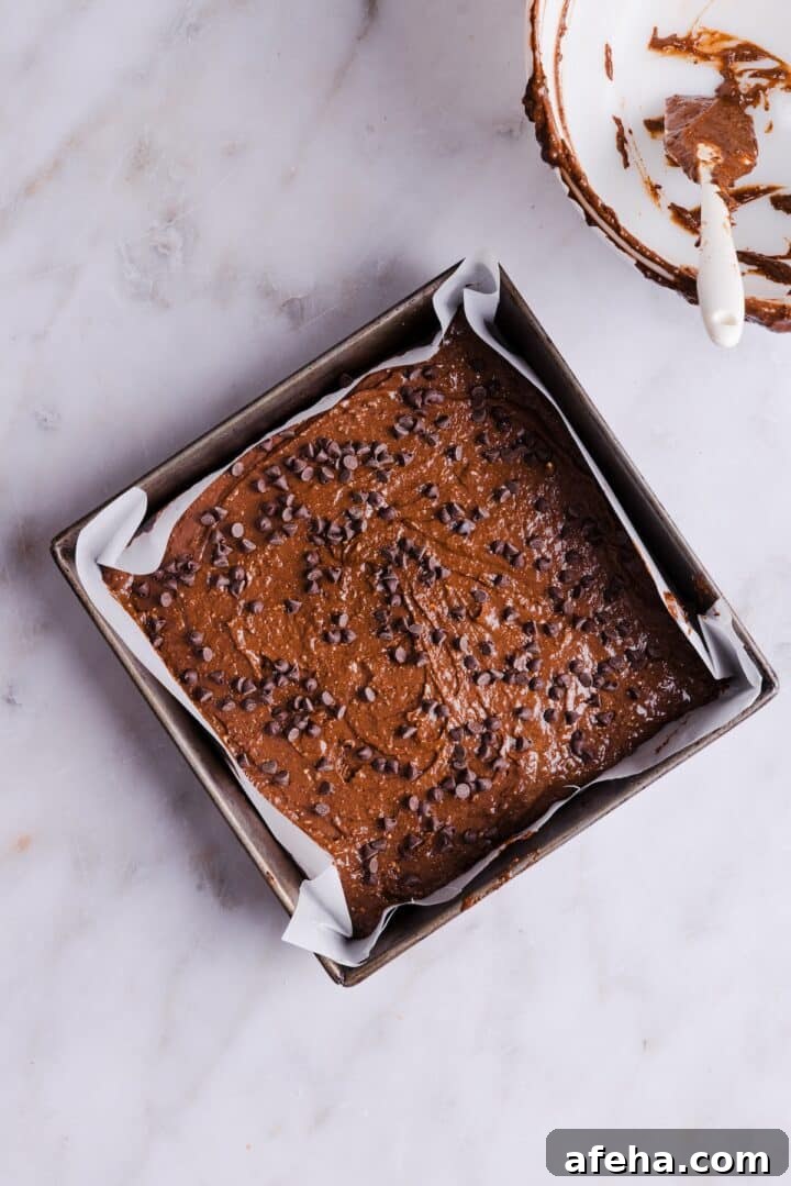 Mini chocolate chips added to raw brownie batter in a square brownie pan