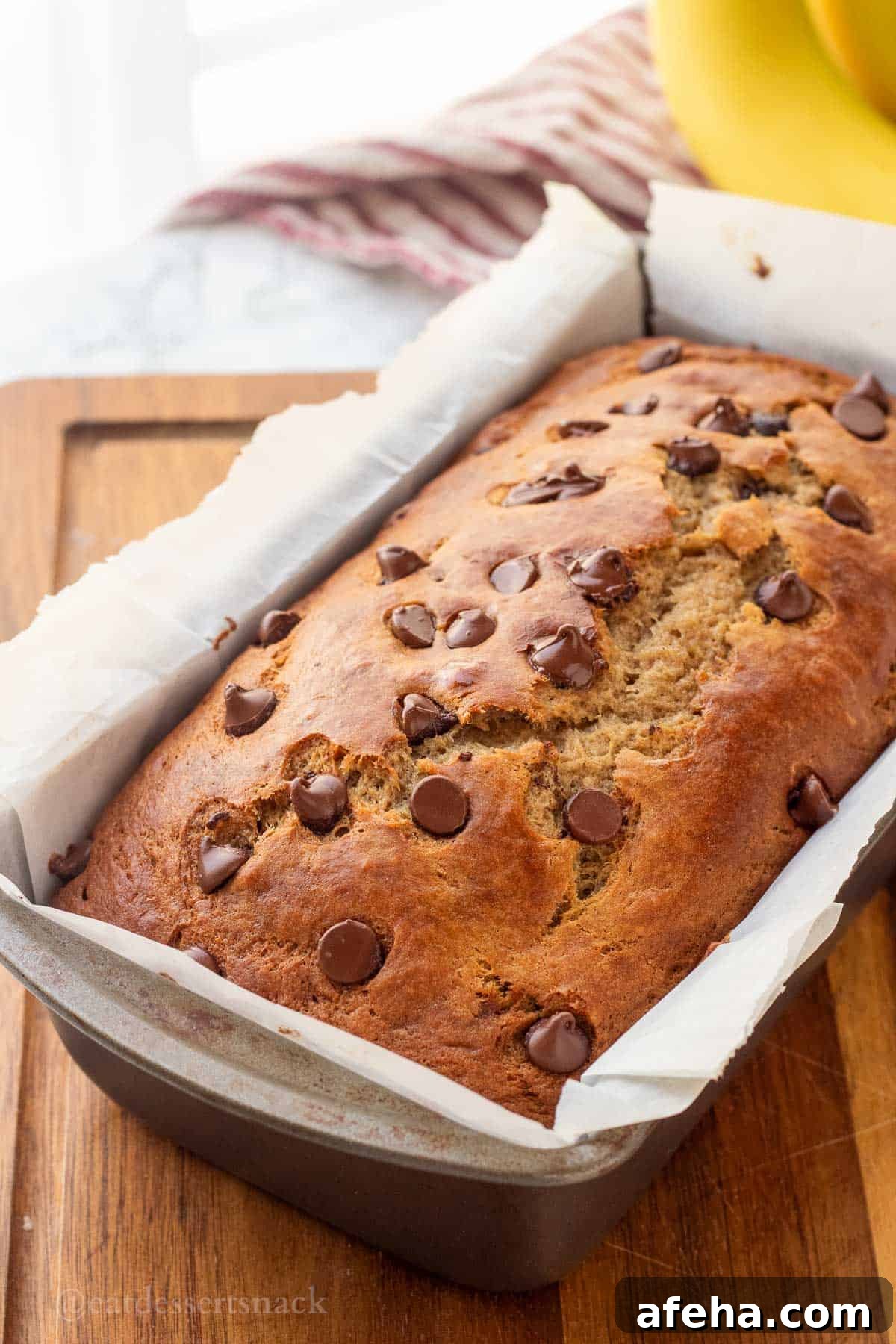 Baked sourdough banana bread in metal pan with chocolate chips on top.