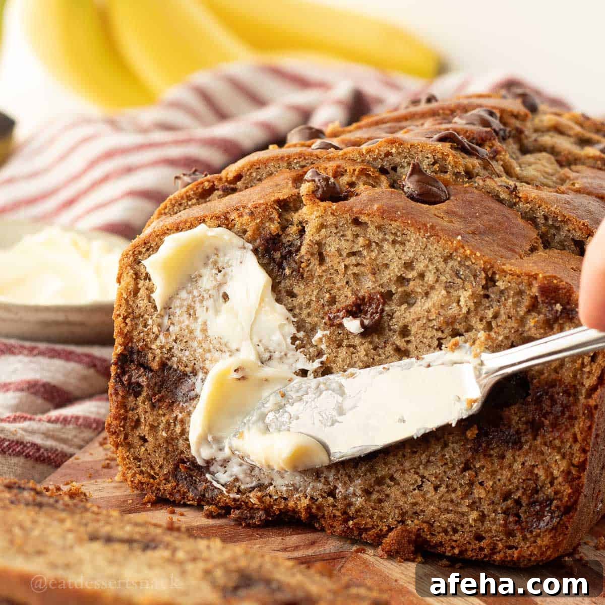 Knife spreading butter over sliced of baked sourdough discard banana bread.