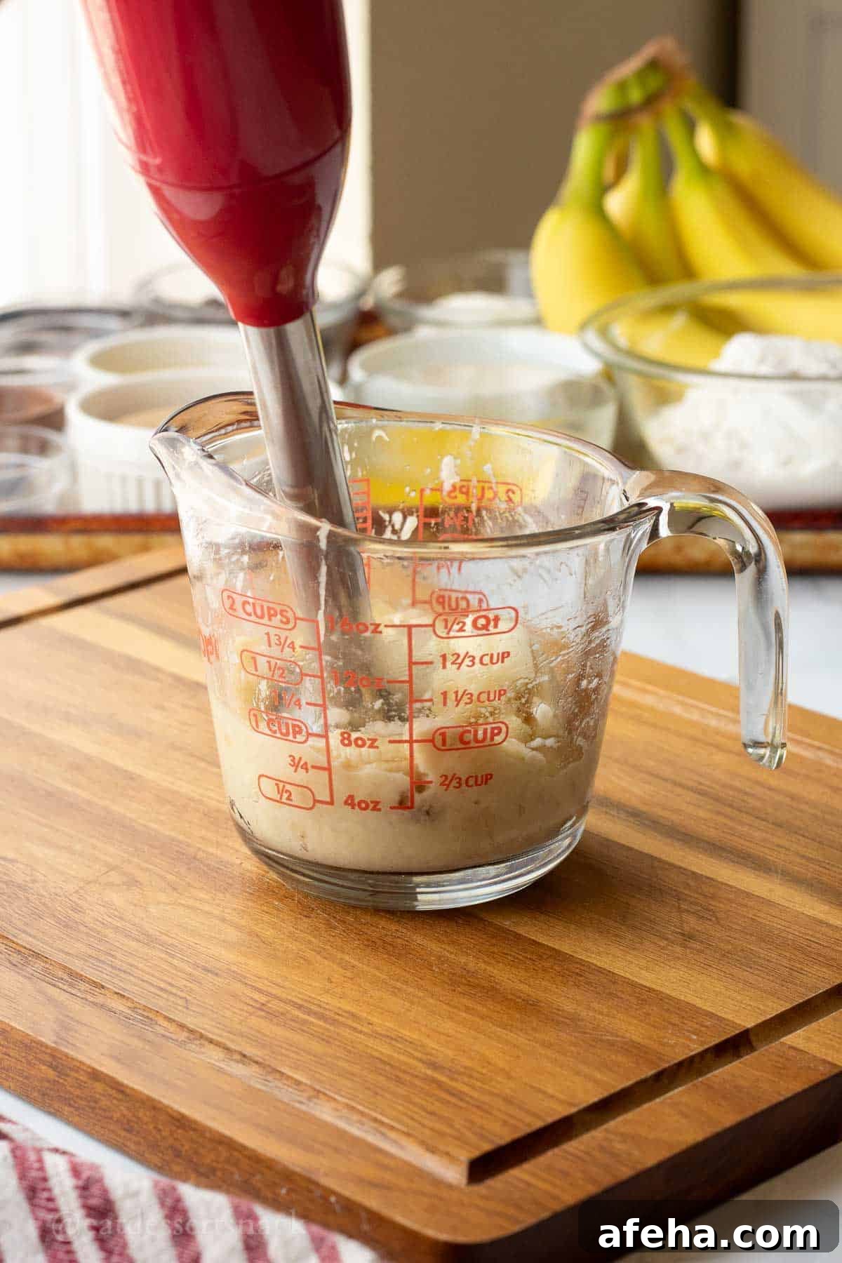 Mashing banana with immersion blender in glass measuring cup.
