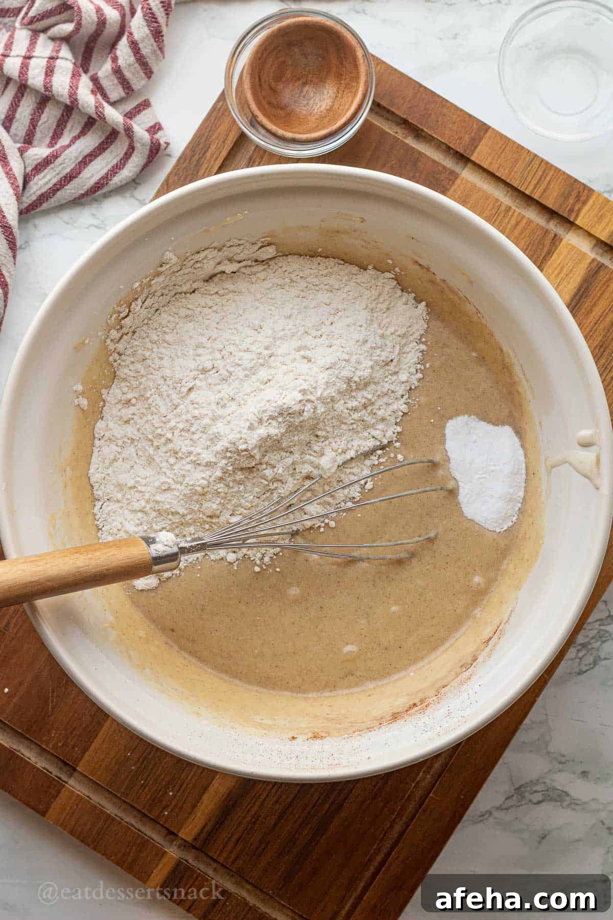 Flour and baking soda over wet banana bread batter in white bowl.