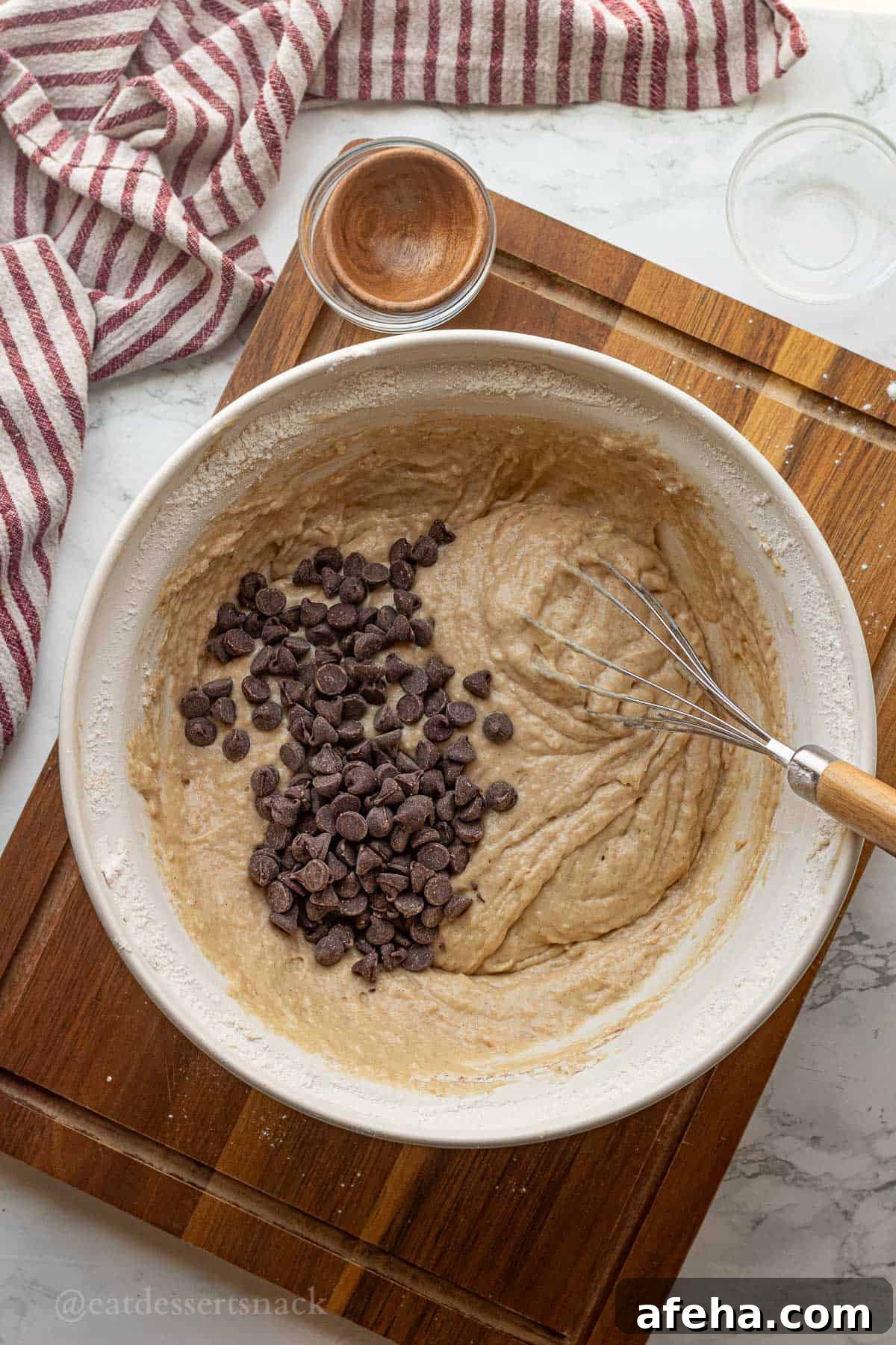 Chocolate chips in raw banana bread batter with whisk in white bowl.