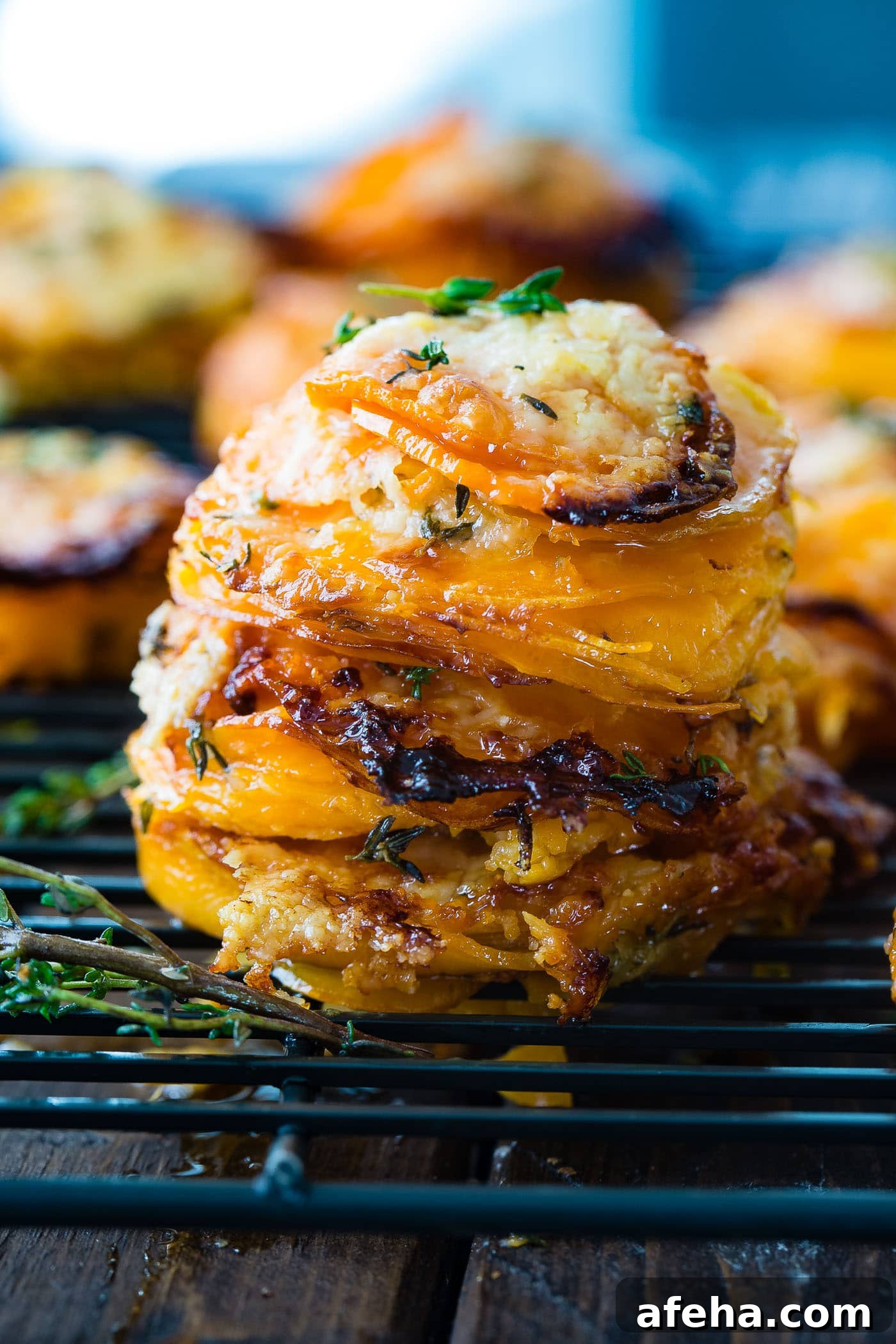 A photo of a stack of thinly sliced sweet potatoes layered with gruyere and parmesan cheese and topped with fresh thyme.